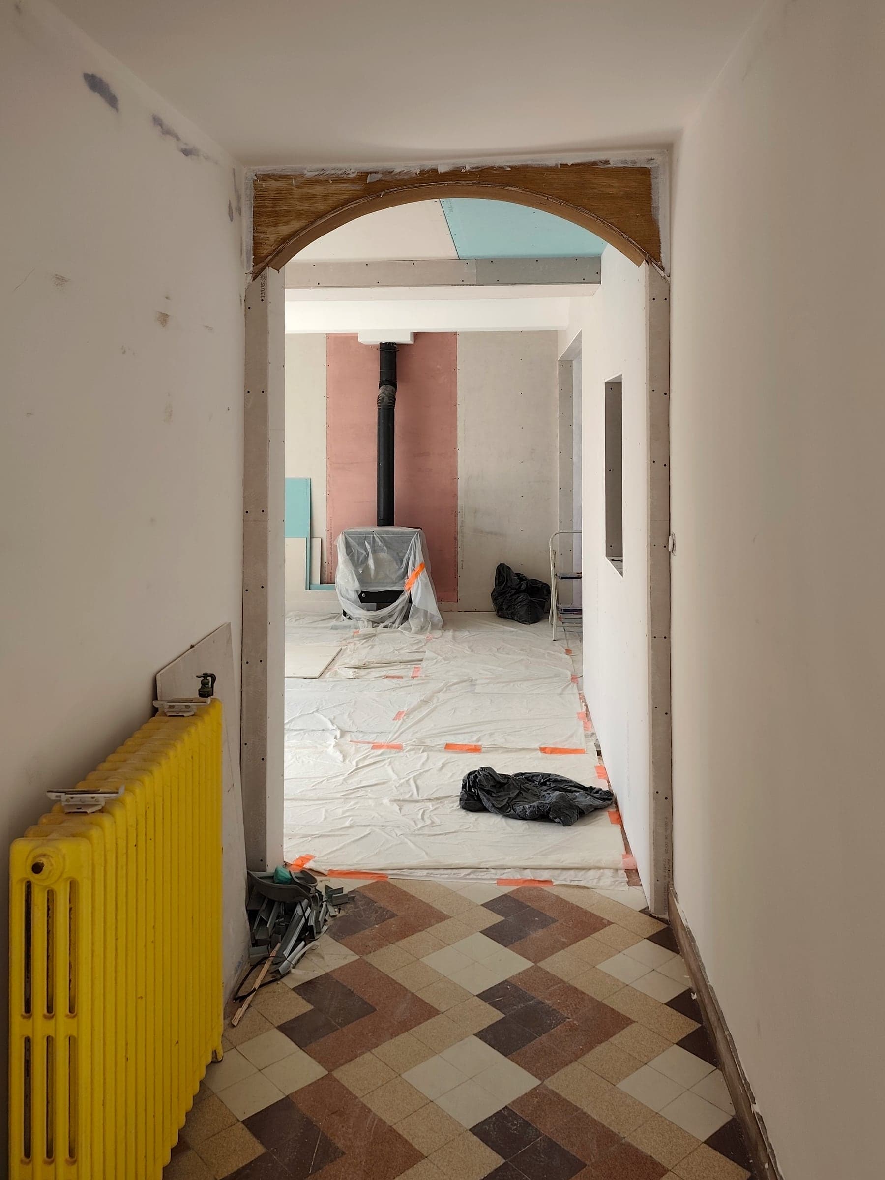 Couloir doublé avec radiateurs jaunes, carrelage ancien et arc de brique au fond
